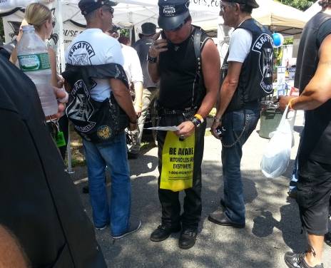 A biker holding a yellow bag advertising motorcycle lawyers and motorcycle awareness. The bags is full of giveaways