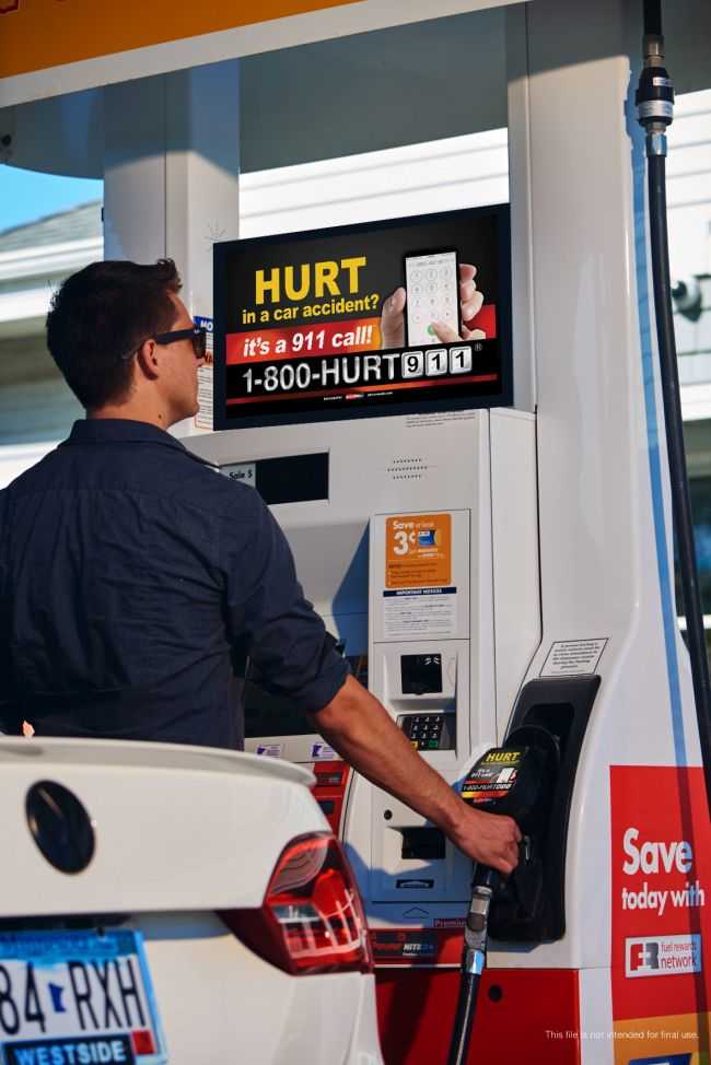 A man pumping gas while looking at a sign on the gas pump advertising personal injury lawyers with the vanity number 1-800-HURT-911® and on the gas nozzle handle.